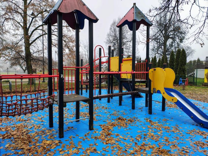 A playground with colorful equipment, including a slide and climbing structures, surrounded by fallen leaves on a blue surface.