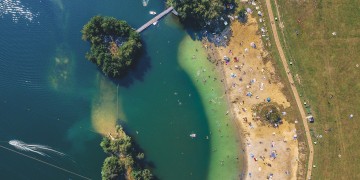 Widok z lotu ptaka na jezioro otoczone lasem z kawałkiem piaszczystej plaży.