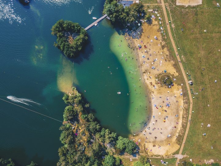 Widok z lotu ptaka na jezioro otoczone lasem z kawałkiem piaszczystej plaży.